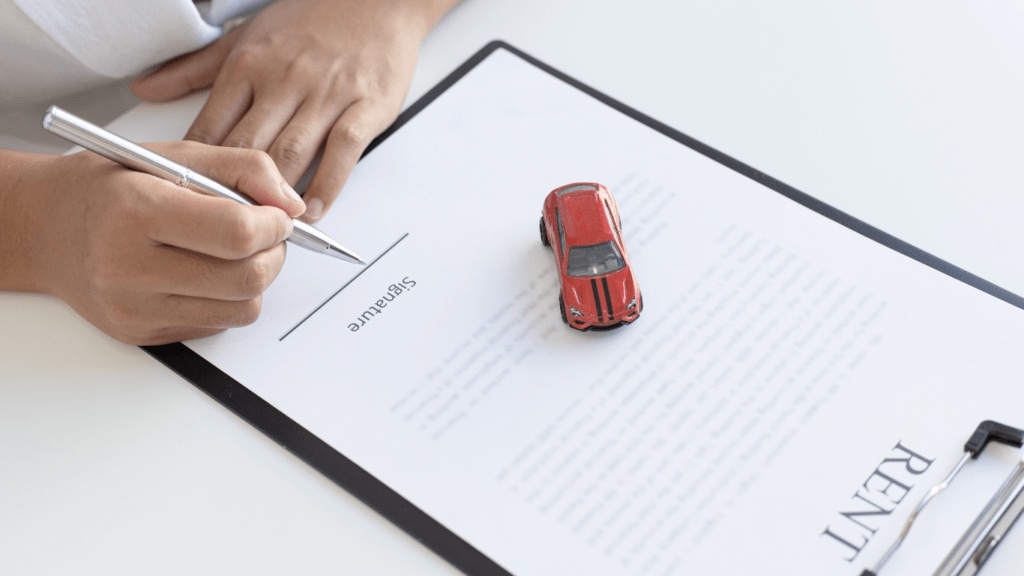 A person is signing a rental agreement with a pen and a toy car