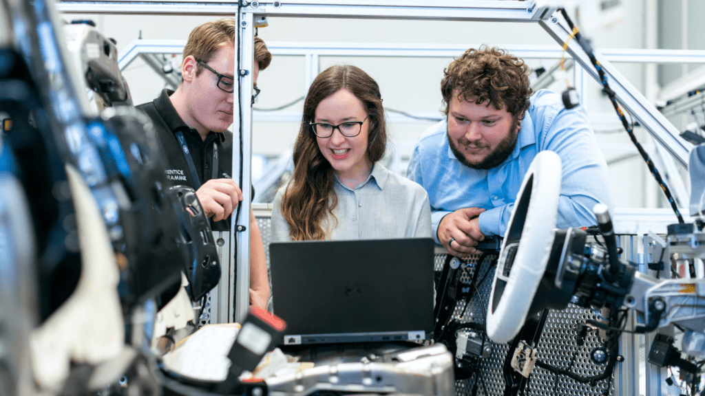 three people working on a laptop in a factory