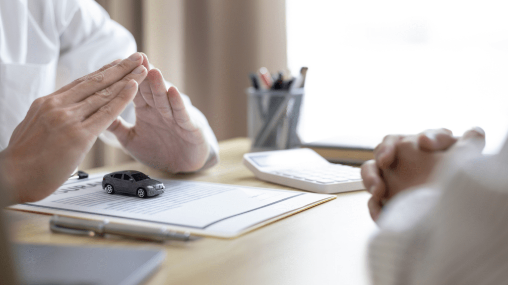 Two people sitting at a desk with a car on the table.