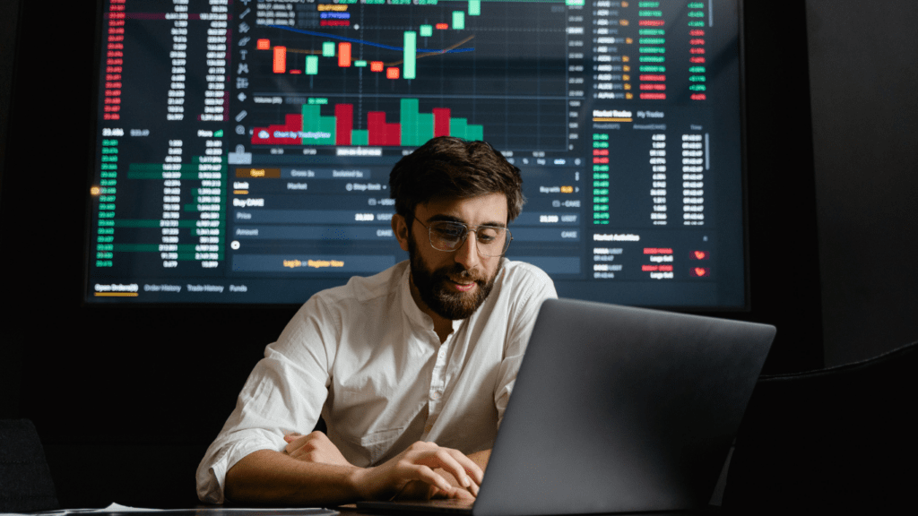 a person sitting in front of a laptop computer with stock market information on the screen