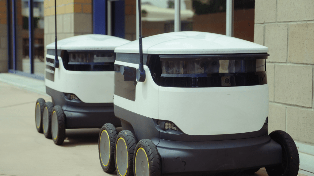 Two self-driving robots are parked on the sidewalk