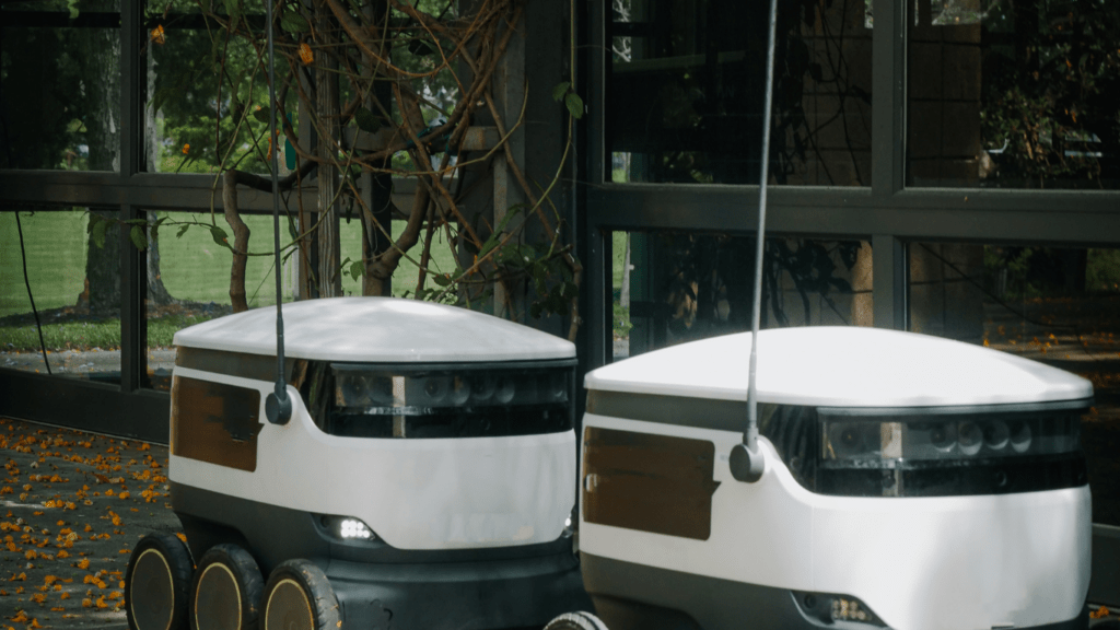 Two self-driving robots are parked on the sidewalk